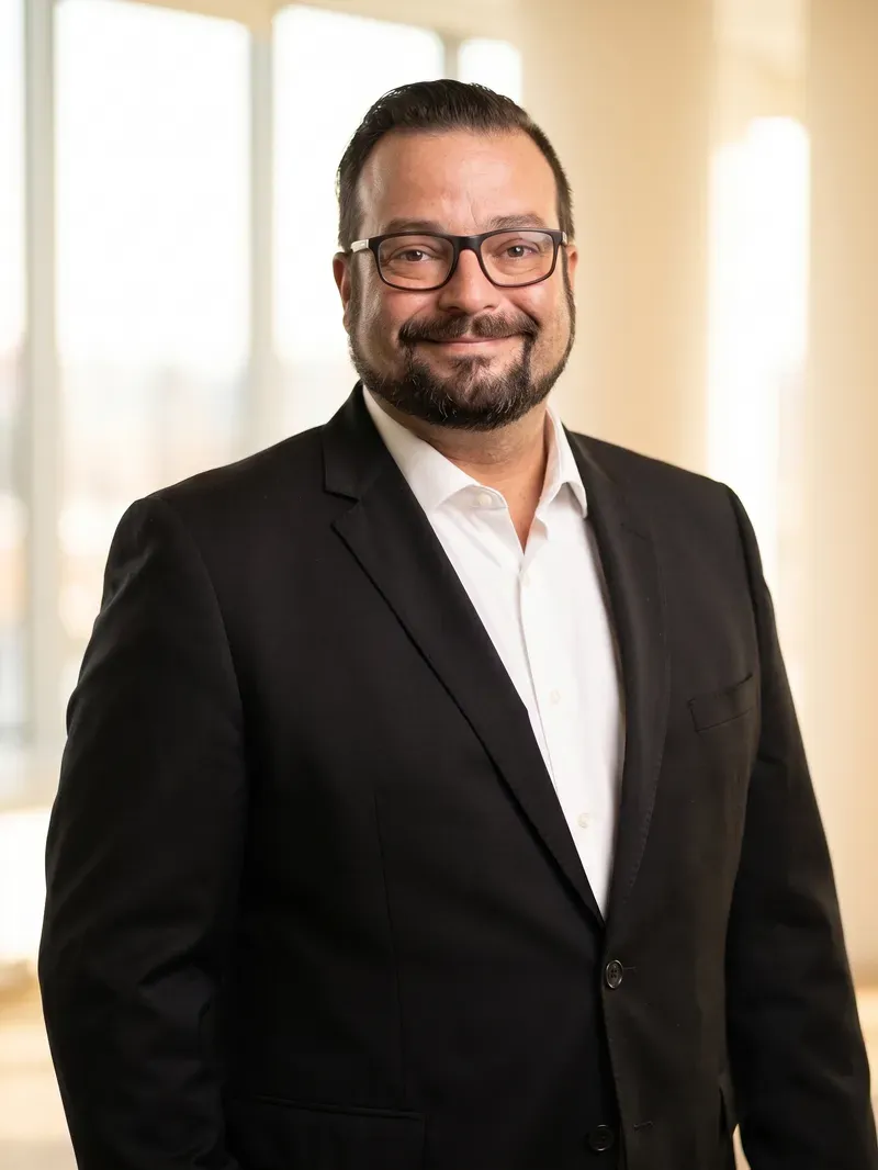 Tiago Santos, wearing a dark blazer and glasses, with warm natural light behind him.